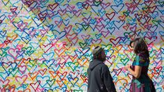 two people standing in front of a wall with hearts painted on it