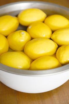 a white bowl filled with lemons on top of a wooden table