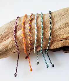 three different colored bracelets on top of a piece of driftwood with wood sticks