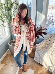 a woman standing in front of a window wearing a red and white cardigan sweater