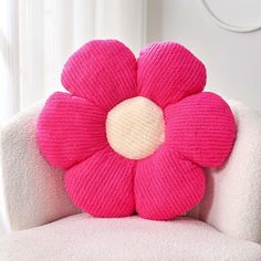 a pink knitted flower sitting on top of a white chair next to a window