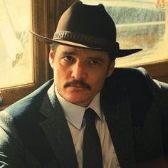 a man in a suit and tie with a mustache wearing a fedora looking at the camera