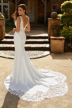 a woman in a white wedding dress standing on a stone walkway with her back to the camera