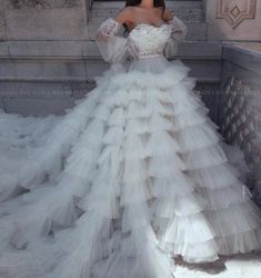 a woman in a white wedding dress standing on a bridge with her arms behind her back