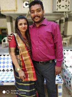 a man and woman standing next to each other in front of a building with colorful tiles on the walls