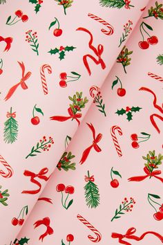 a pink christmas wrapping paper with holly, candy canes and candies on it