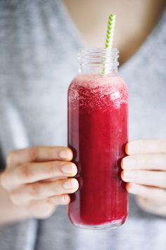 a woman holding a glass with a red drink in it and a green straw sticking out of the top