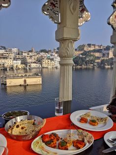 plates of food are sitting on an outdoor table overlooking the water and cityscape