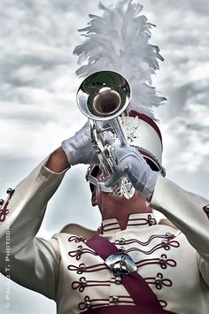 a man in white and red uniform playing a trumpet with feathers on his head while looking into the distance