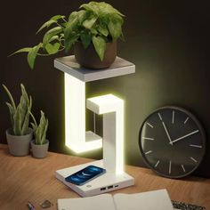 a table with a clock, plant and cell phone on it next to an open book