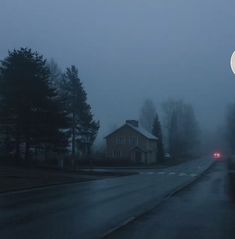 a foggy street with a red car on the road and houses in the background