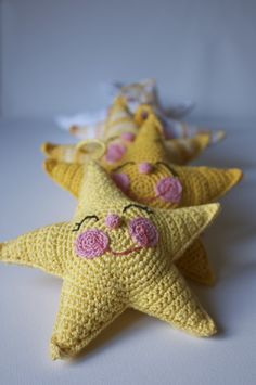 three crocheted yellow stars with pink flowers on them, one is smiling and the other has eyes closed