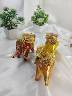 three small glass elephants sitting on top of a white tablecloth covered table next to potted plants