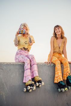 two women sitting on the edge of a skateboard ramp, one holding a camera