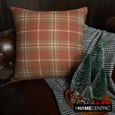 a plaid pillow and christmas tree on a leather chair with a wooden tray holding pine cones