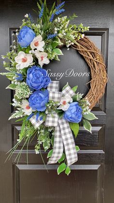 a wreath with blue flowers and greenery is hanging on the front door to welcome guests