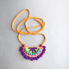 a colorful necklace is hanging on a yellow cord with beads and bead work in the shape of a flower