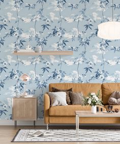 a living room with blue floral wallpaper and a tan couch in front of a coffee table