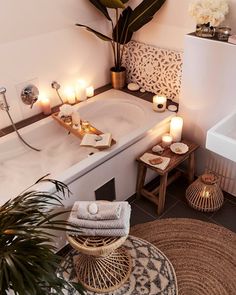 a bathtub with candles and towels on the floor next to a sink in a bathroom