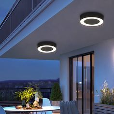 an outdoor dining area with white chairs and round lights on the ceiling, overlooking a city at night