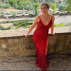 a woman in a red dress standing on a ledge with her hands out and looking at the camera