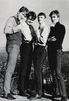 four young men standing next to each other in front of a bush and sky background