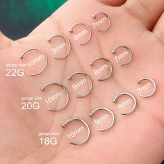 six pairs of small silver hoop earrings on a person's hand with measurements for each pair