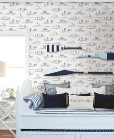 a white bed sitting under a window next to a wallpaper covered in blue and white