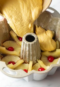 someone is pouring batter into a cake pan with pineapples and cherries on it