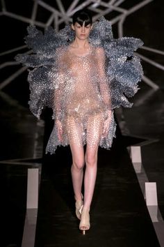 a woman walking down a runway wearing a dress made out of plastic beads and feathers