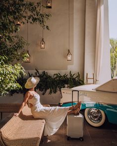 a woman in a white dress and hat sitting on a bench next to a car