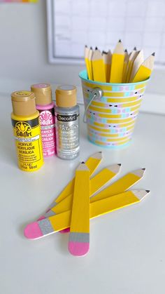 some pencils and markers are sitting on a table next to a cup full of pens