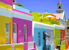 brightly colored houses line the street in an urban area with white buildings and colorful umbrellas