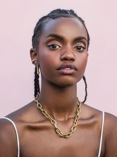 a woman with braids wearing a gold chain necklace on her neck and looking off to the side