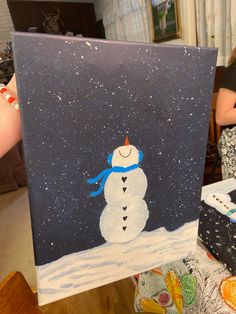 a painting of a snowman is being held up by someone's hand in the living room