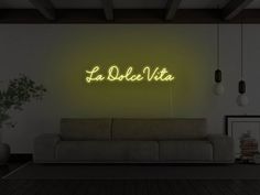 a living room with a couch and neon sign on the wall that says la dolce vita