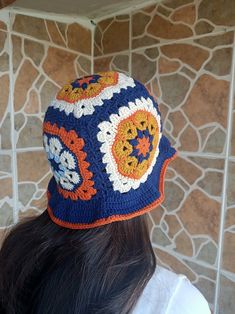 a woman is wearing a crocheted hat in front of a wall with rocks