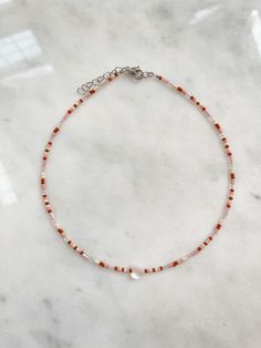 This dainty Seed Bead Choker Necklace, Anklet, & Ring is made with pretty multicolor glass seed beads. Light pink, terracotta/red & cream seed beads are used in this set which create a warm look. The tiny seed beads are strung on beading wire & finished with a stainless steel lobster style clasp with a 2 inch extension chain, to allow for personal size adjustments. Enjoy a simple, colorful look with a single strand or layer them with some of our other chokers. * Each set will come wi Adjustable Orange Beaded Necklaces With Heart Beads, Adjustable Orange Beaded Necklace With Heart Beads, Pink Bohemian Tiny Beaded Necklace, Orange Heart Beads For Jewelry Making, Red Seed Bead Necklace, Seed Bead Necklace Pink, Red Choker With Tiny Beads, Pink Heart-shaped Jewelry With Tiny Beads, The Tiny Seed