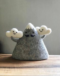 two little felt clouds sitting on top of a wooden table next to a gray wall