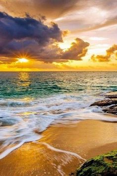 the sun is setting over the ocean with waves crashing on the shore and rocks in the foreground