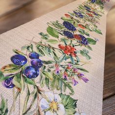 an embroidered table runner with flowers and leaves on the side, sitting on top of a wooden table