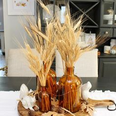 two brown vases filled with wheat sitting on top of a wooden tray next to shells