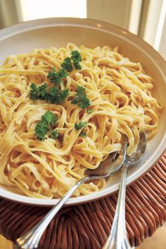 a white bowl filled with pasta and parsley on top of a wicker place mat