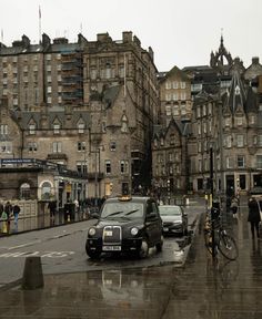 a black car driving down a wet street next to tall buildings and people walking on the sidewalk