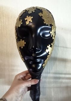 a person holding up a black mask with gold puzzle pieces on it's face