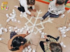 three children are sitting on the floor making snowflakes out of cups and water bottles