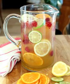 a pitcher filled with lemons and raspberries next to sliced oranges on a cutting board