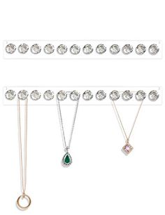 three different necklaces hanging on a white wall with diamonds and emerald pendants in the middle