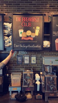 a man holding up a sign in front of a coffee shop with breakfast items on display