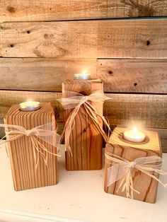 three wooden candle holders with lit candles in them sitting on a white table next to wood planks